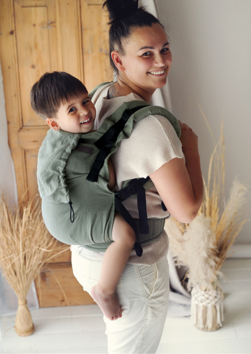 Lachende ouder draagt een kind op de rug in de groene Little Frog Preschooler Pure Linen Grove draagzak.