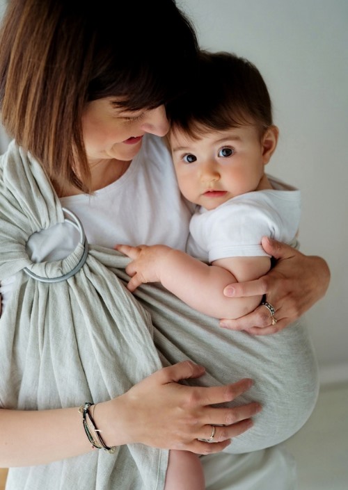 Moeder draagt baby in licht grijsgroene ringsling met zilverkleurige ringen