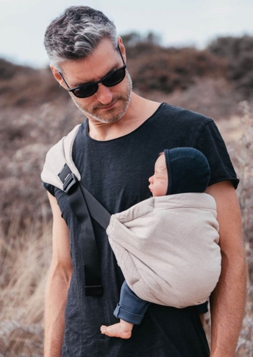 Man draagt baby in lichtbeige Hoppediz Hip-Hop Hip Carrier met brede zwarte schouderband