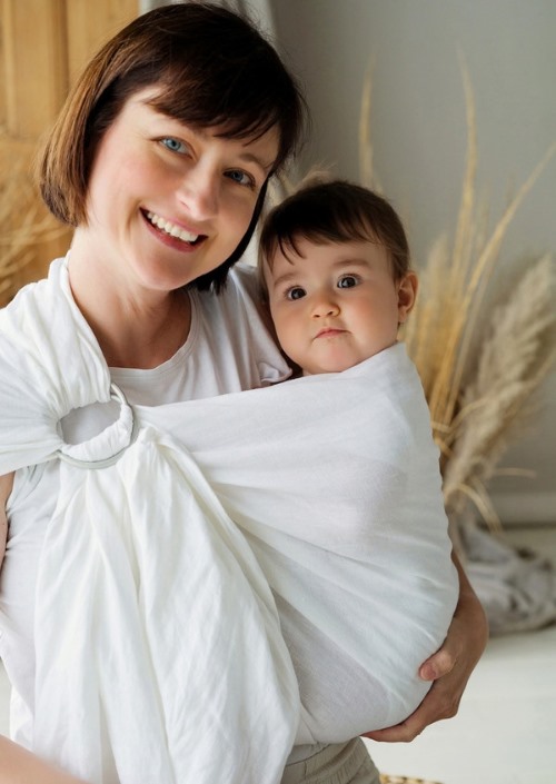 Vrouw draagt baby in witte Little Frog ringsling met zichtbare ringen op de schouder