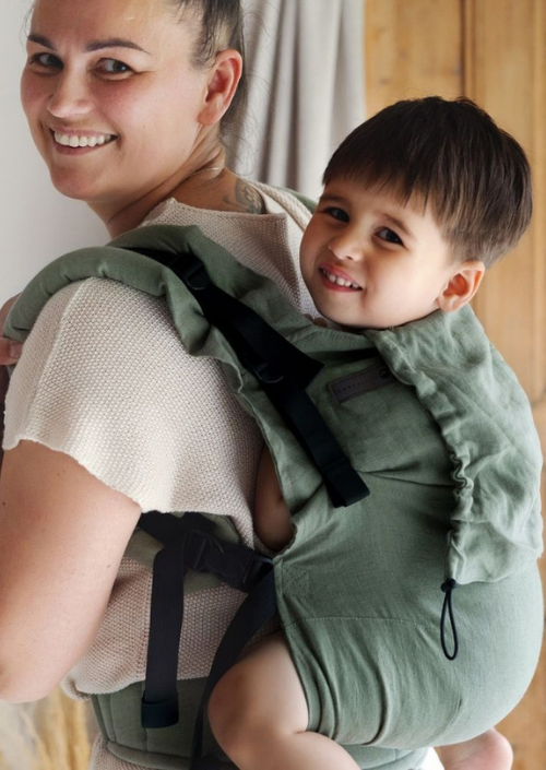 Kind kijkt over de schouder vanuit de groene Little Frog Preschooler Pure Linen Grove draagzak.