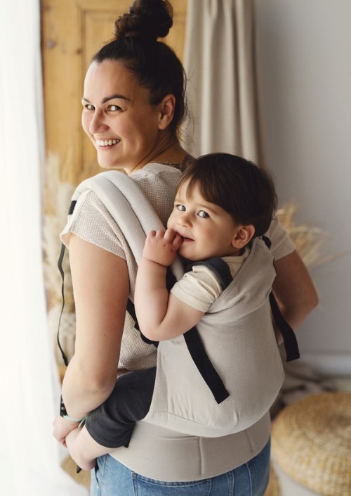 Beige Little Frog Swift Toddler Carrier met zwart detail, gedragen op de rug met een peuter