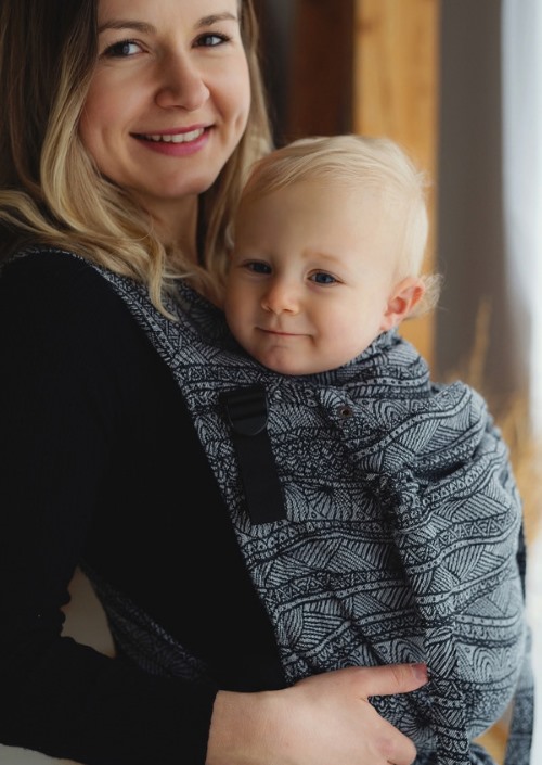 Moeder draagt baby in grijs-zwarte Little Frog Cross Hybrid Carrier met geometrisch patroon