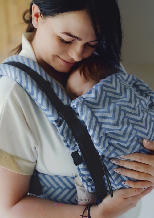 Vrouw draagt baby in blauw-wit zigzagpatroon draagzak met zwarte schouderbanden