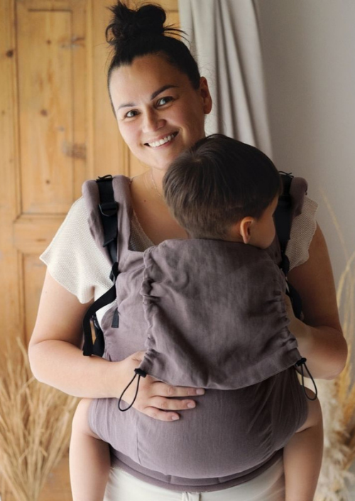 Ouder draagt een kindje op de buik in de Little Frog Preschooler Pure Linen draagzak in een warme lichtbruine kleur.