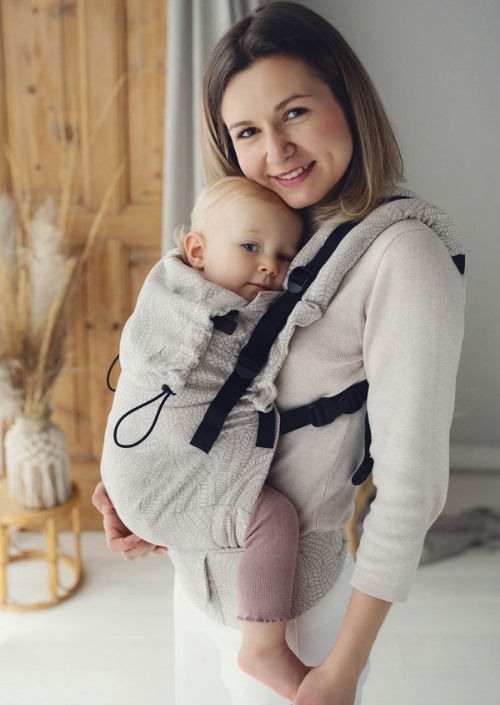 Moeder draagt baby in lichtgrijze Little Frog Prime Carrier met subtiel bladpatroon en zwarte gespen