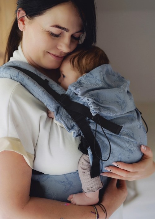 Moeder draagt baby in lichtblauwe Little Frog draagzak met donkerblauwe bloemprint en zwarte gespen