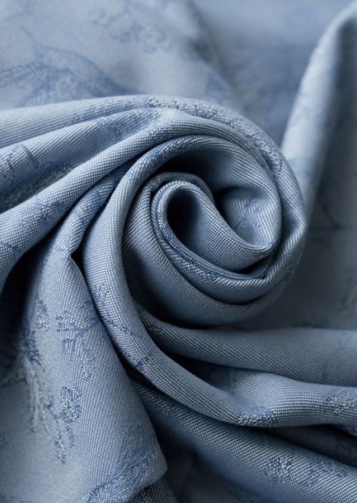 Lichtblauwe ringsling met ingeweven subtiel bloemmotief, opgerold in close-up