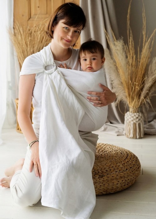 Vrouw draagt baby in witte ringsling met ring op de schouder
