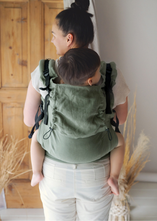 Ouder draagt een kind op de rug in de groene Little Frog Preschooler Pure Linen Grove draagzak, van achteren gefotografeerd.