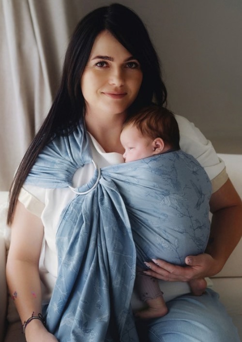 Moeder draagt baby in lichtblauwe Little Frog-ringsling met subtiel ingeweven patroon en zilverkleurige ringen