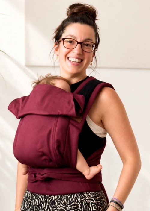 Vrouw draagt een baby in de bordeauxrode Hoppediz Bondolino b.pure buikdrager met brede schouderbanden.