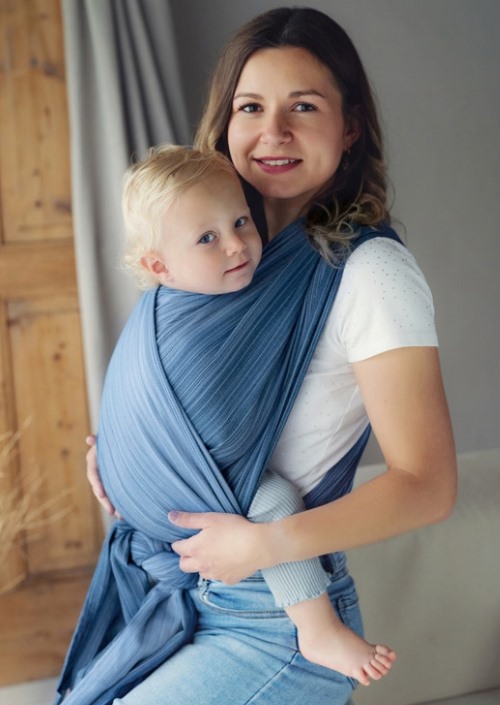 Moeder draagt kind in blauwgrijze Little Frog Bamboo Celestine draagdoek, vooraan geknoopt rond de taille