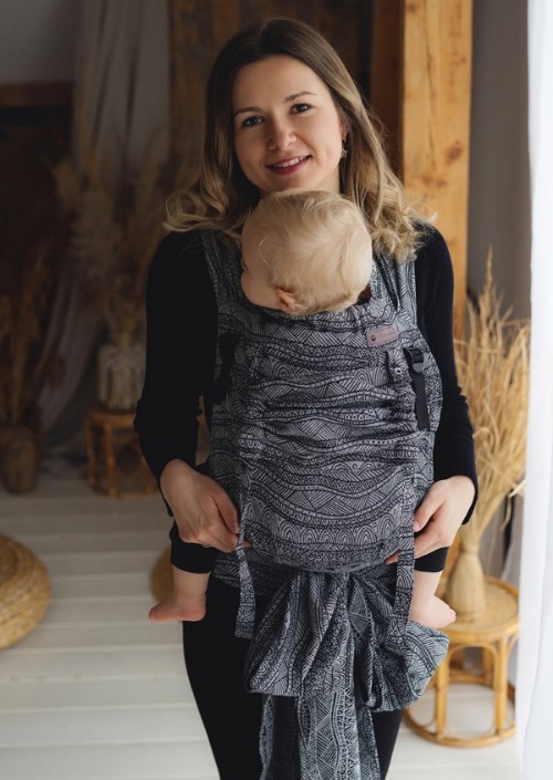 Little Frog Cross Hybrid Carrier Carbon Harmony met zwart-wit golvend patroon, gedragen met baby op de buik