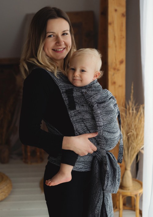 Moeder draagt baby in Little Frog Cross Hybrid Carrier met grijszwart bladpatroon.