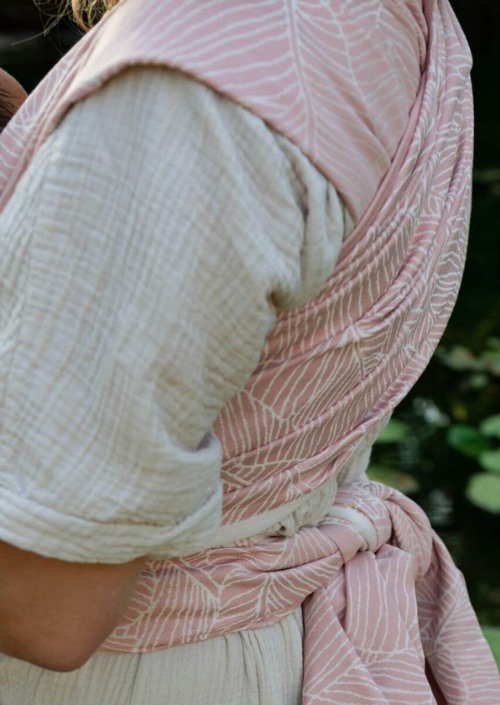 Roze Hoppediz Grenada Rose draagdoek met wit bladerenpatroon, geknoopt rond de taille gedragen