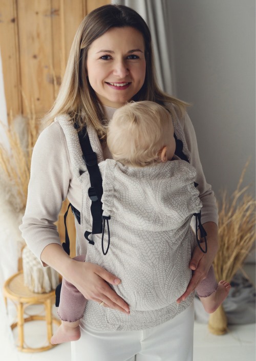 Vrouw draagt een baby in Little Frog Prime Carrier Natural Wildness met licht bladpatroon en zwarte gespen