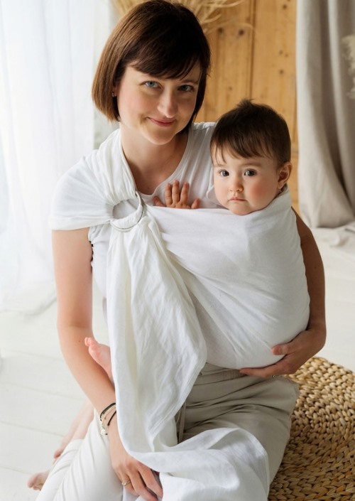Vrouw draagt baby in witte Little Frog ringsling met ringen op de schouder