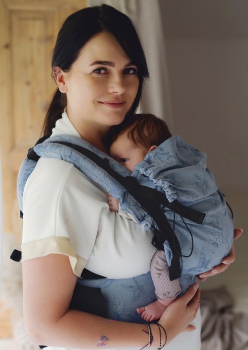 Vrouw draagt baby in lichtblauwe Little Frog Prime Carrier met subtiel dessin en zwarte gespen
