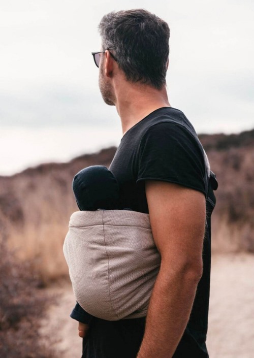 Man draagt een baby in een lichtbeige Hoppediz Hip-Hop Hip Carrier buiten in zijaanzicht