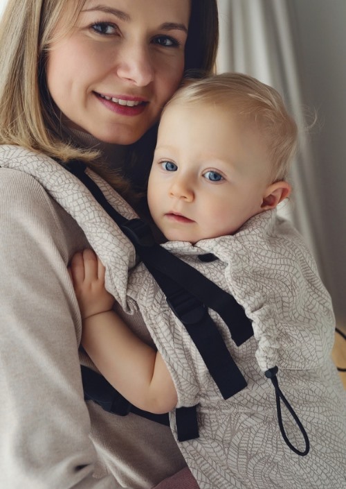 Baby in Little Frog Prime Carrier Natural Wildness met licht bladpatroon en zwarte gespen, gedragen door een vrouw