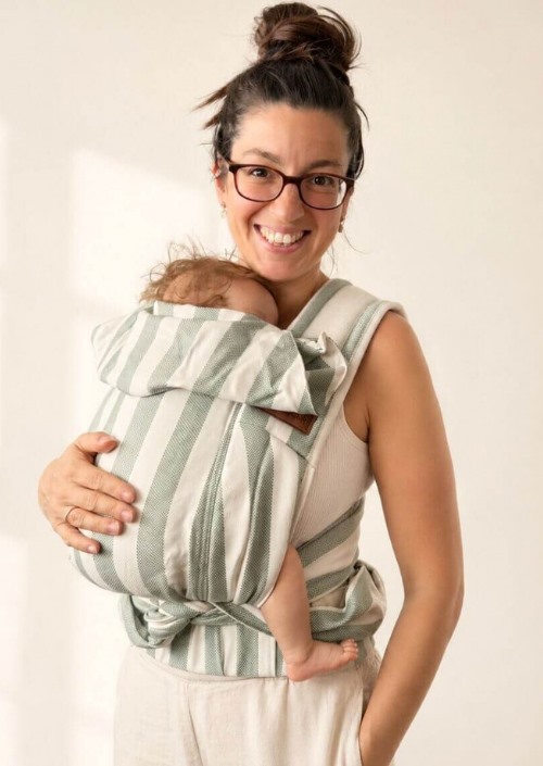 Vrouw draagt een baby in Hoppediz Bondolino b.pure Matcha Latte met groen-witte strepen en capuchon