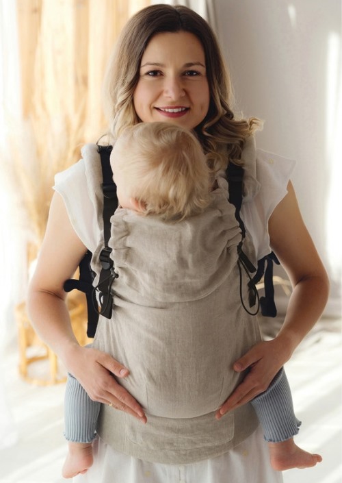 Vrouw draagt baby op de buik in beige Little Frog Prime draagzak met zwarte gespen en banden