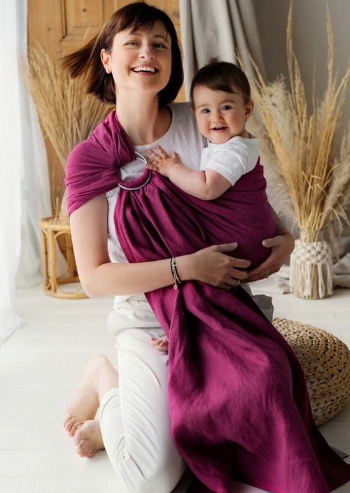 Moeder draagt baby in paarse Little Frog ringsling met zichtbare ringen op de schouder