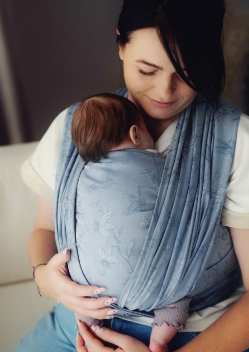 Moeder draagt baby in lichtblauwe Little Frog draagdoek met ingeweven bloemenpatroon