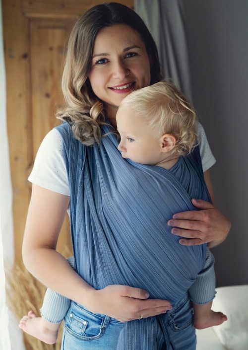 Vrouw draagt een kind op de buik in een lichtblauwe geweven draagdoek.